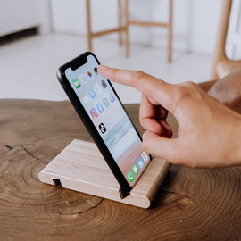 Zeigefinger der rechten Hand tippt auf ein Smartphone, das in einer Halterung auf einem Tisch steht.